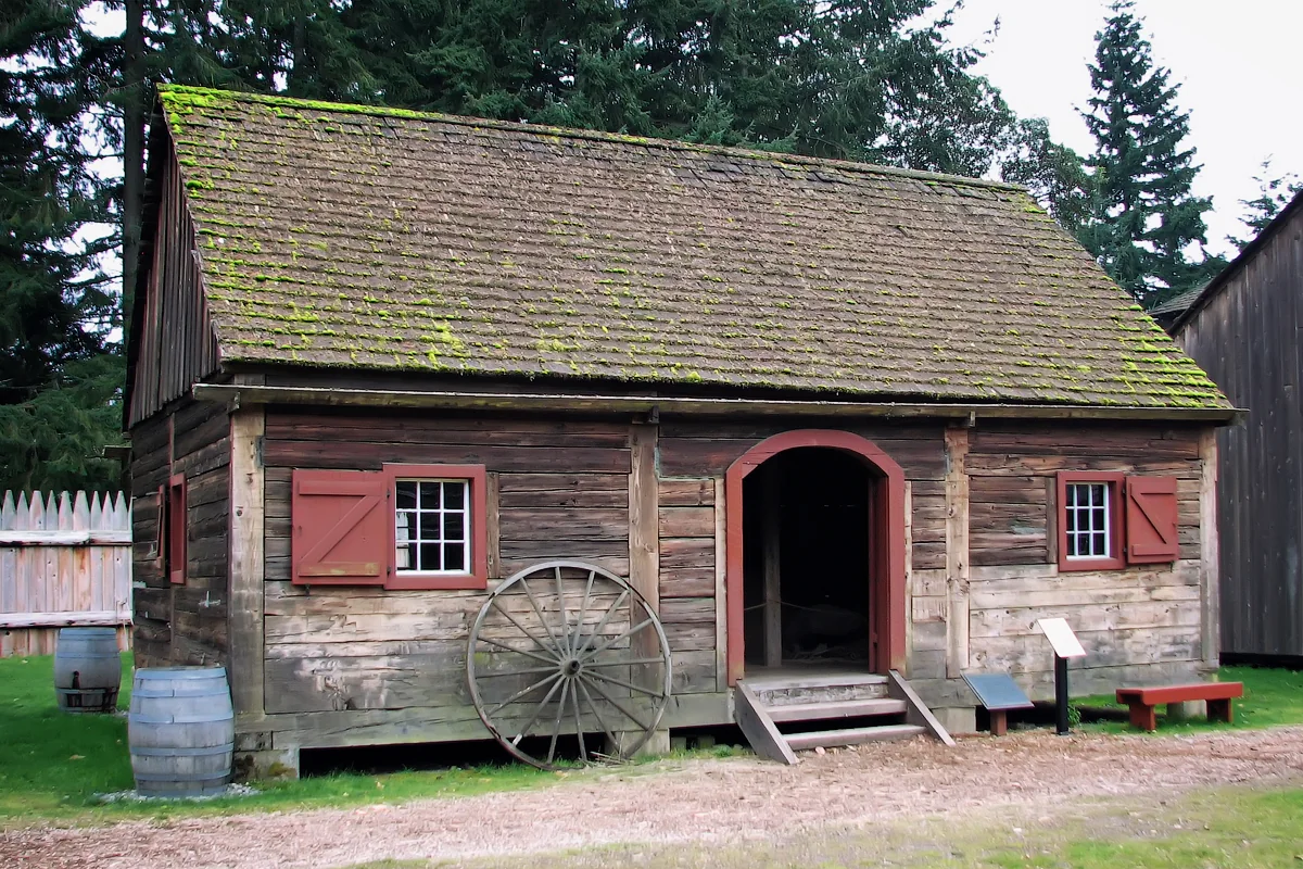 The weathered timber granary at Fort Nisqually, with red window frames and moss on its roof.