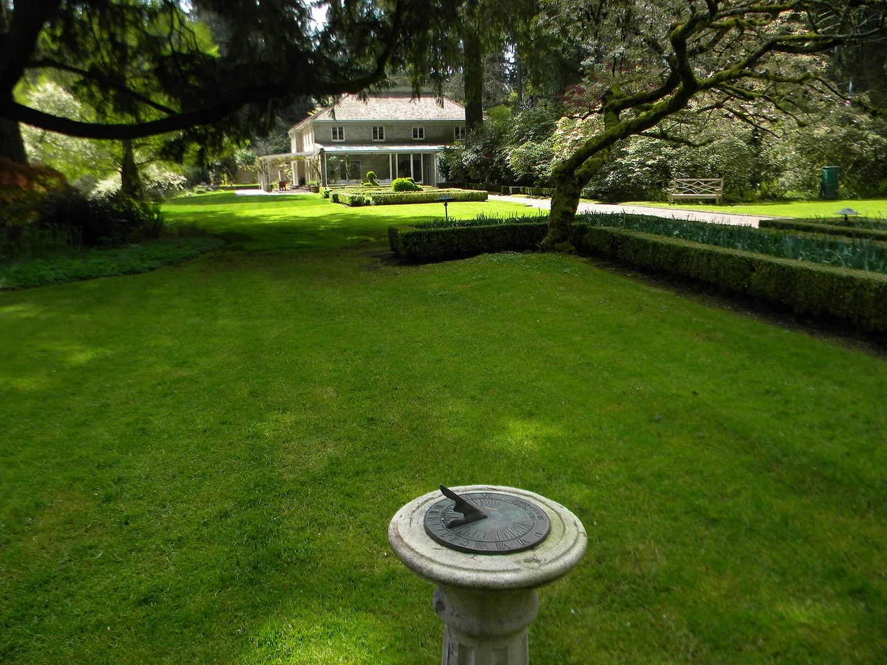 Spreading tree branches frame a green lawn, birdbath and the house at Lakewold Gardens.